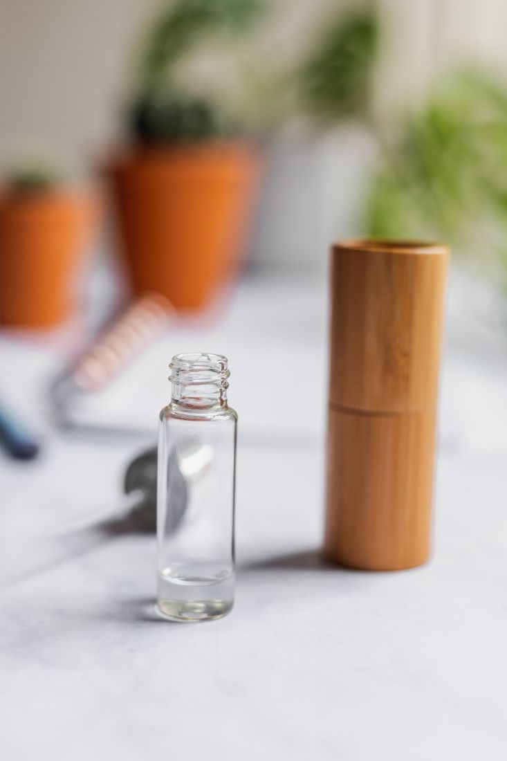 Kleine leere Sprühflasche ohne Verschluss neben Bambushalter mit im Hintergrund Verschluss und Pflanzen